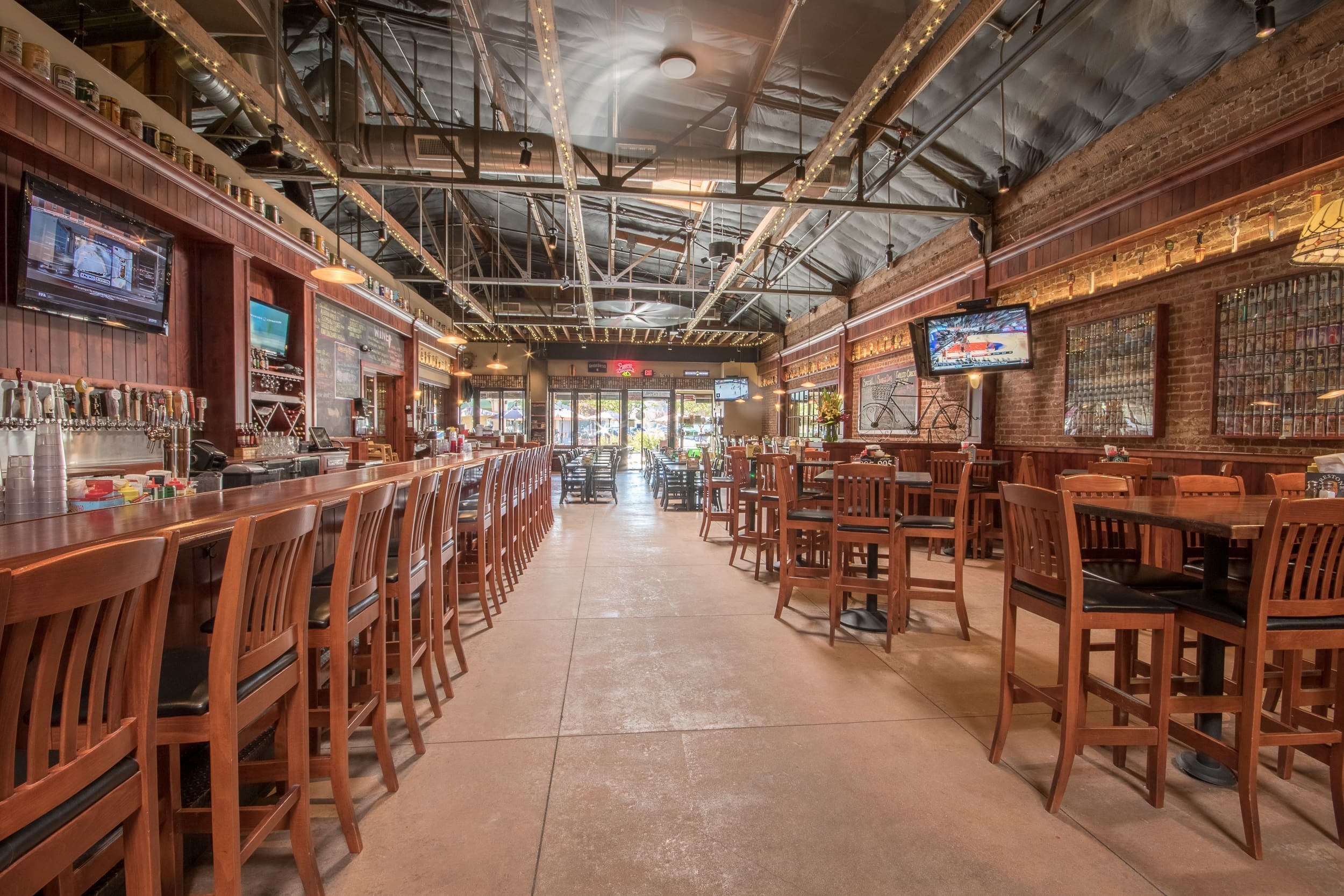 Interior of First Street Alehouse with long wooden bar, taps, brick wall, and dining tables.